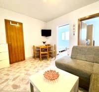 Obývací pokoj v rodinném domě s pohovkou, stolkem a televizí na stěně.