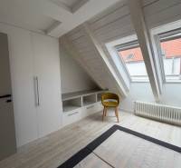 Podkrovní pokoj s podlahou s dřevěným dekorem, vestavěnou skříní a žlutou židlí.