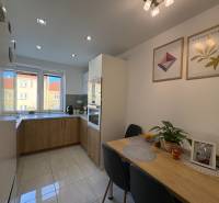 Kuchyně v 2-pokojovém bytě, světlá dlažba, stůl s dekoracemi, obrázky na stěně.