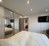 Ložnice v 2-pokojovém bytě s televizí, velkou skříní a podlahou s dřevěným dekorem.