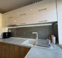 Kuchyně v 2pokojovém bytě se světlými skříňkami a podsvícením nad pracovní deskou.