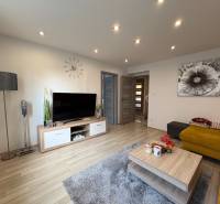 Obývací pokoj v 2-pokojovém bytě s podlahou s dřevěným dekorem, TV a žlutou pohovkou.