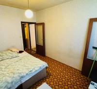 Ložnice s kobercem, postelí a světlými stěnami v dvoupokojovém bytě.