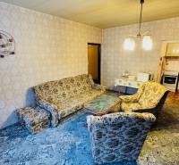 Obývací pokoj s retro sedací soupravou, vzorovaný koberec, vstup do kuchyně v 2-pokojovém bytě.