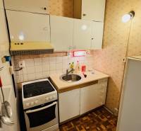 Kuchyně v 2-pokojovém bytě, bílé skříňky, sporák, dřez, podlaha s dřevěným dekorem.