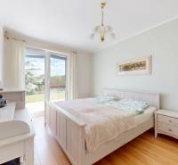 Ložnice v rodinném domě s podlahou s dřevěným dekorem a výhledem do zahrady.