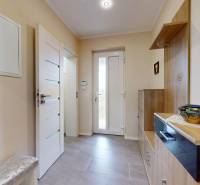 Vstupní hala rodinného domu s dlažbou, dekorativními obrazy a úložným prostorem.