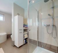 Koupelna v rodinném domě s vanou, sprchovým koutem a úložnými policemi.