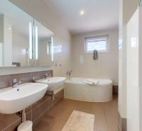 Koupelna v rodinném domě s dvojitým umyvadlem, vanou a keramickými obklady.