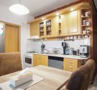 Kuchyně ve 3-pokojovém bytě se světlou kuchyňskou linkou, spotřebiči a stolem se židlemi.