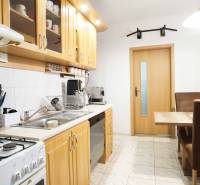 Kuchyně ve 3-pokojovém bytě s dřevěnými skříňkami a jídelním stolem.