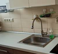 Kuchyně v 2-pokojovém bytě s dřezem, sklokeramickou varnou deskou a košíkem u okna.