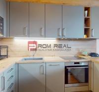 Kuchyně s podlahou dřevěného dekoru, vestavěnými spotřebiči a nástěnnými skříňkami v 2pokojovém bytě.