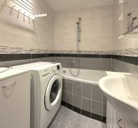 Koupelna s vanou, pračkou a dlažbou v 2-pokojovém bytě.
