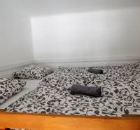 Manželská postel s dekorativním ložním prádlem a bílými stěnami.