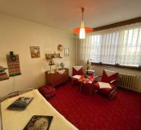 Pokoj v 3-pokojovém bytě se starším nábytkem, červeným kobercem a dekoracemi.