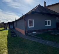 Rodinný dům v Mýtných Ludanech, obklopený zahradou, s modrou oblohou a sluncem.