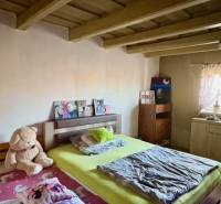 Ložnice v rodinném domě s dřevěným stropem, postelí a plyšovým medvědem.