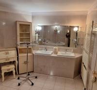 Koupelna v rodinném domě se dvěma umyvadly, zrcadlem a zdobeným nábytkem.