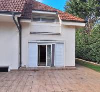 Rodinný dům v Komárně s terasou, zahradou a bílými okenicemi.