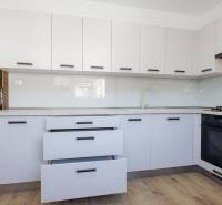 Kuchyně v 3-pokojovém bytě s bílými skříňkami a podlahou s dřevěným dekorem.