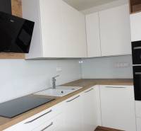 Kuchyně s bílými skříňkami a spotřebiči, doplněná podlahou s dřevěným dekorem v 3pokojovém bytě.