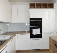 Moderní kuchyně s bílými skříňkami a podlahou s dřevěným dekorem v 3pokojovém bytě.