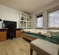 Pokoj v 2-pokojovém bytě s postelí, pracovním stolem a podlahou s dřevěným dekorem.