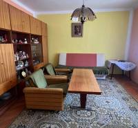 Obývací pokoj v rodinném domě s retro nábytkem, zelenými křesly a velkým kobercem.