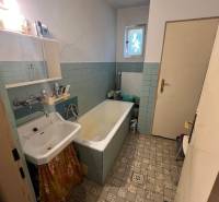 Koupelna v rodinném domě se starou vanou, umyvadlem a dlažbou.