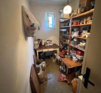 Úložný prostor v rodinném domě s regály plnými různých předmětů a otevřeným oknem.