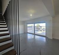 Obývací pokoj ve vile s moderním schodištěm a velkými okny.