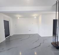 Prostorná místnost ve vile s bílými stěnami a šedou podlahou s dekorem.