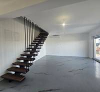 Interiér vily s kovovým schodištěm a podlahou s dřevěným dekorem, velké okno na terasu.