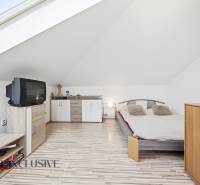 Podkrovní ložnice s televizí, postelí a skříněmi v rodinném domě.