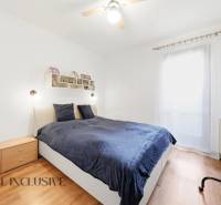 Ložnice v rodinném domě s postelí, dřevěným dekorem podlahy a televizorem na stěně.