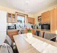 Kuchyně v rodinném domě s dřevěným dekorem nábytku a vybavením, květinová dekorace na stole.