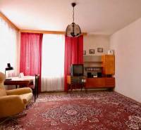 Obývací pokoj v rodinném domě s červeným kobercem, křeslem a závěsy na oknech.