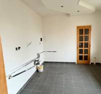 Prázdná místnost v 2-pokojovém bytě, podlaha z tmavé dlažby, bílé stěny, dřevěné dveře.