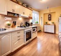 Kuchyně v 2-pokojovém bytě s podlahou s dřevěným dekorem, světlá linka a rostliny.