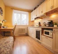 Kuchyně v 2-pokojovém bytě s dřevěným dekorem podlahy, světlým nábytkem a jídelním koutem.