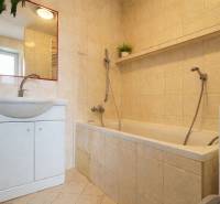 Koupelna v 2-pokojovém bytě s vanou, umyvadlem, zrcadlem a béžovými obklady.