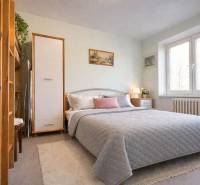 Ložnice v dvoupokojovém bytě s velkou postelí, dekoracemi a naturalistickým osvětlením.