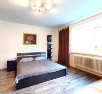 Ložnice v rodinném domě s postelí, skříňkou, obrazem a podlahou s dřevěným dekorem.