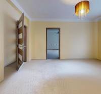 Světlý pokoj v rodinném domě se záclonami, lustrem a otevřenými dveřmi.