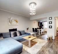 Obývací pokoj s podlahou s dřevěným dekorem, šedou sedačkou a jídelním stolem v rodinném domě.