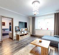 Obývací pokoj v rodinném domě s krbem, podlahou s dřevěným dekorem a sedací soupravou.