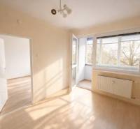 Světlý pokoj s podlahou s dřevěným dekorem propojený s balkónem ve 2pokojovém bytě.