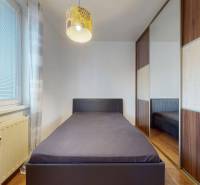 Jednolůžková postel u okna, vestavěná skříň a podlaha s dřevěným dekorem ve 3pokojovém bytě.