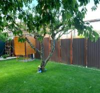 Zahrady v Dolních Krškanech, Nitra, s trávníkem, stromem, malým dřevěným domečkem a plotem.